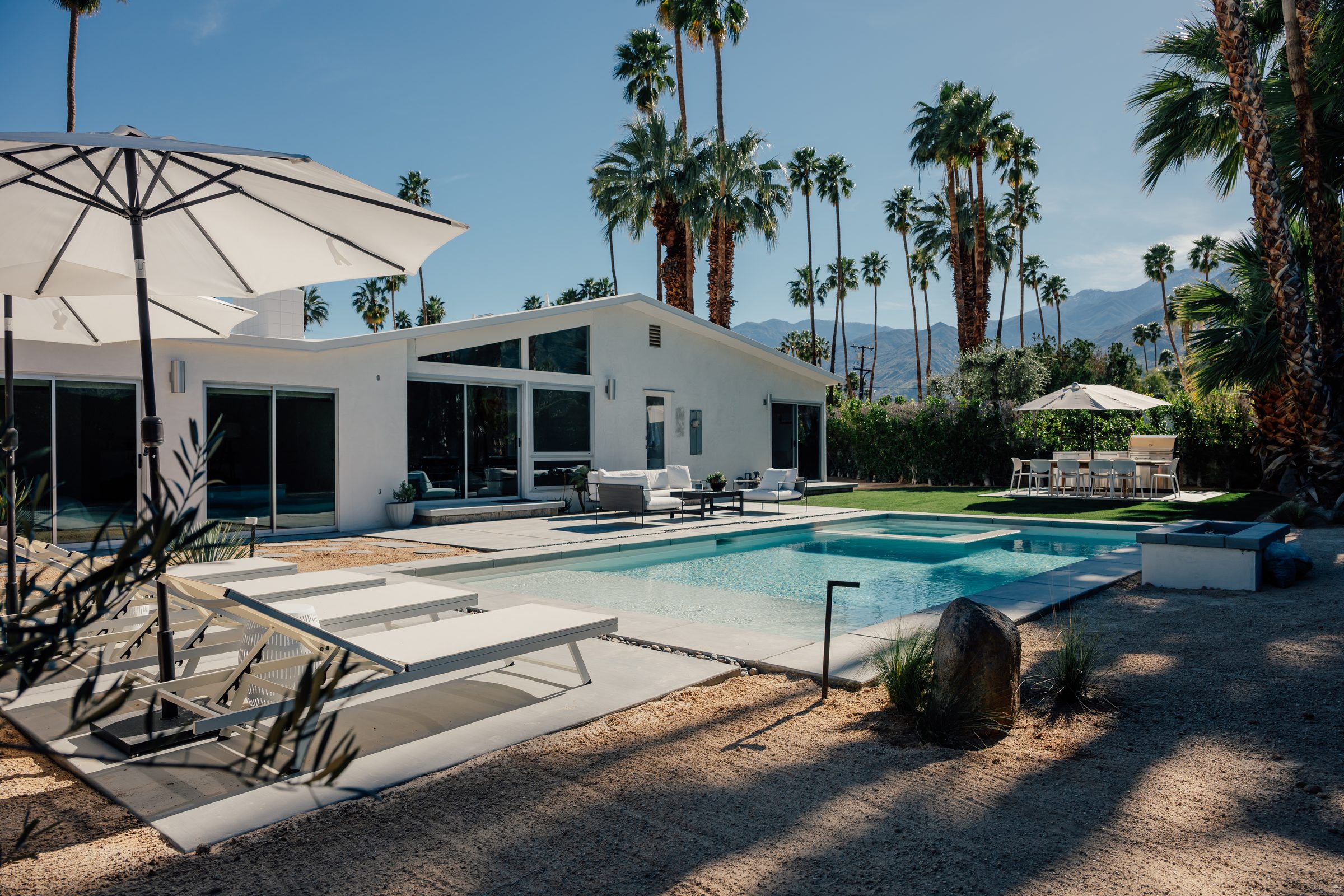 Renovated 1961 Krisel home in Twin Palms, Palm Springs: a gabled glass rear elevation, a new pool and spa, palms, and the San Jacinto mountains beyond